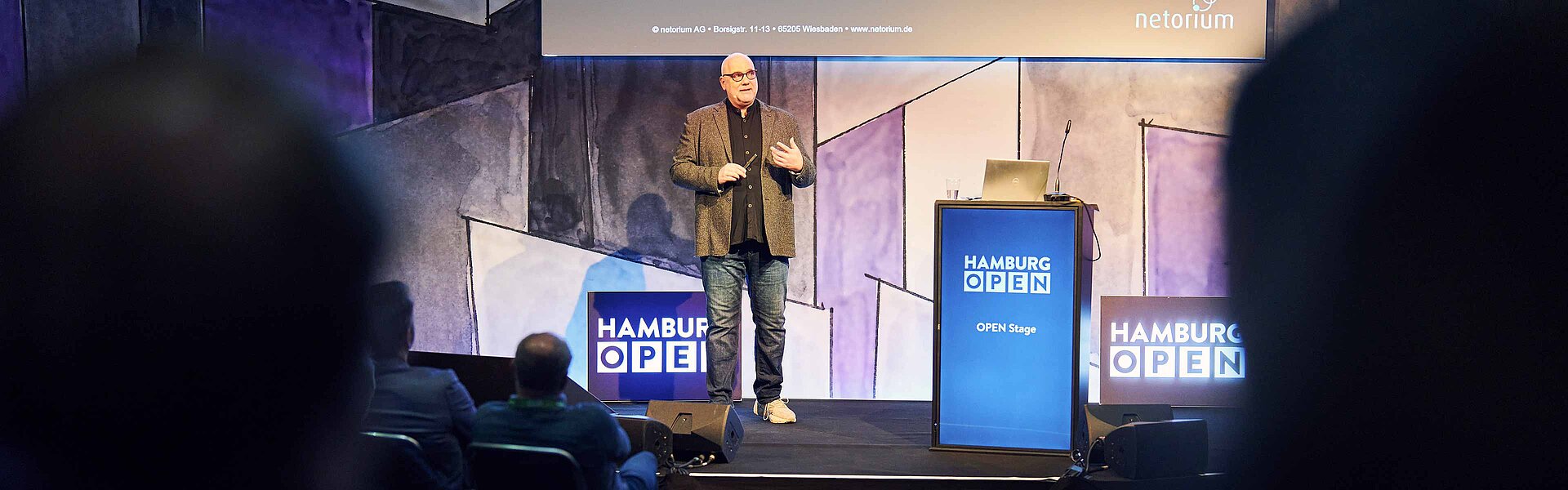 Speaker steht neben seinem Pult auf der OPEN Stage und präsentiert vor Publikum.