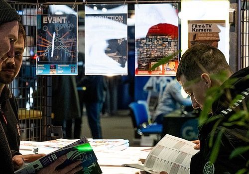 Three people are reading the magazines in the trade press area.