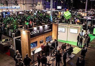 View of the HAMBURG OPEN hustle and bustle in Hall B6. Many people are chatting at the different stands or in the networking area.