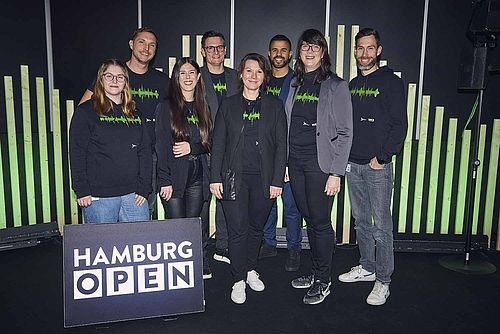 HAMBURG OPEN team. Eight women and men smile into the camera. In front of them there is a sign that says: HAMBURG OPEN.