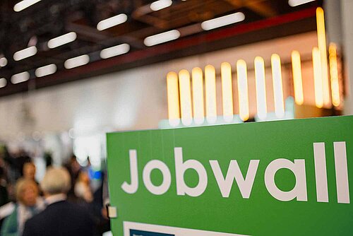 In the foreground is a green sign with the word Jobwall. In the background, visitors can be recognised in a blur.