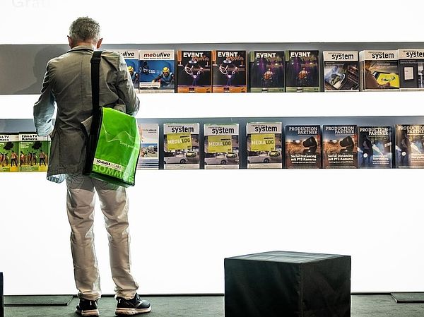 Person stands in front of a white wall with a trade press display.